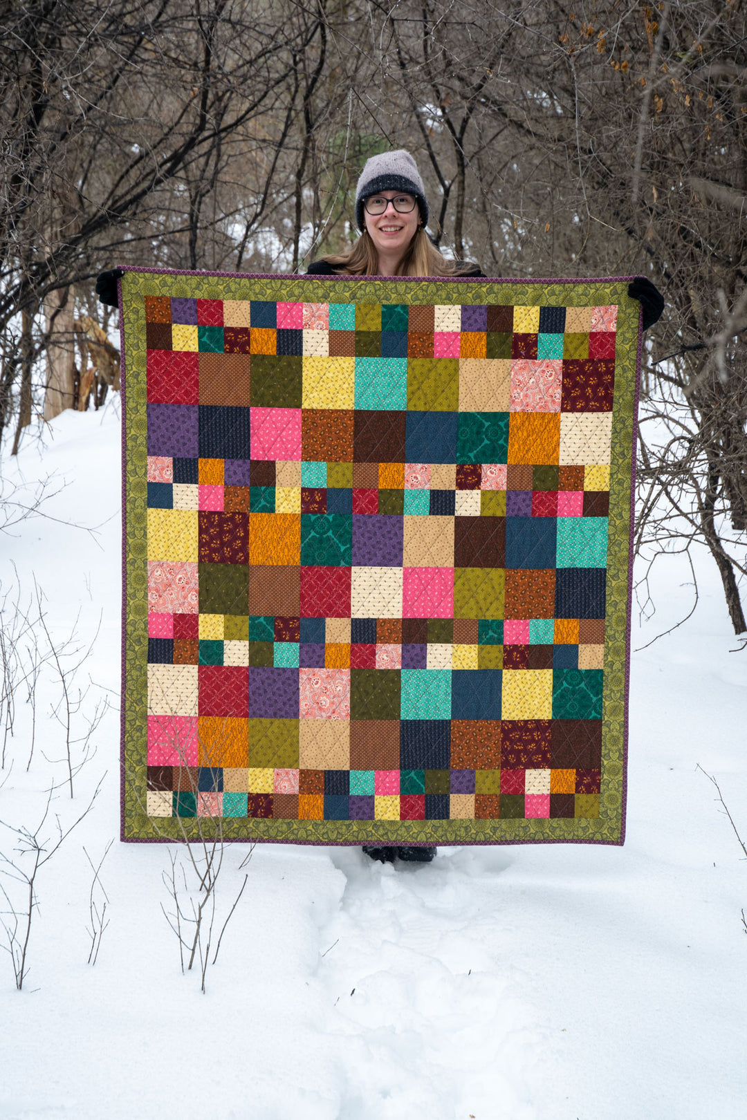 Person holding a colourful quilt in a snowy landscape